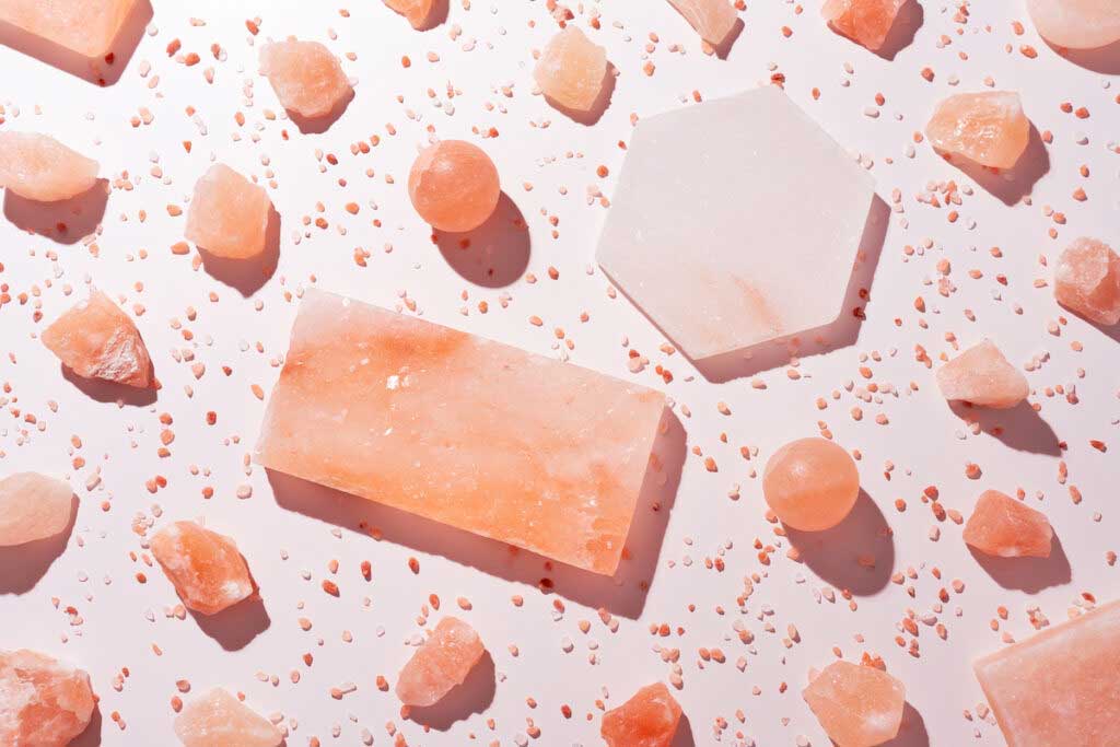 Variously sized and shaped chunks of Himalayan pink salt on a light pink background.