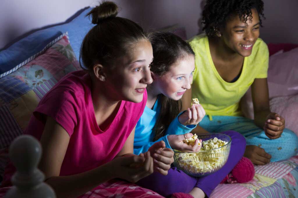 Preteens watch a movie with popcorn at a slumber party.