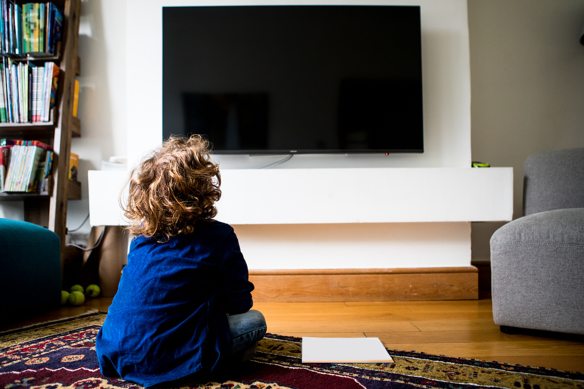 Rear view of a child sitting in front of a blank television screen.
