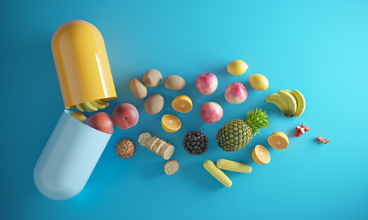 A vitamin capsule opens to reveal fruits and vegetables on a blue background.