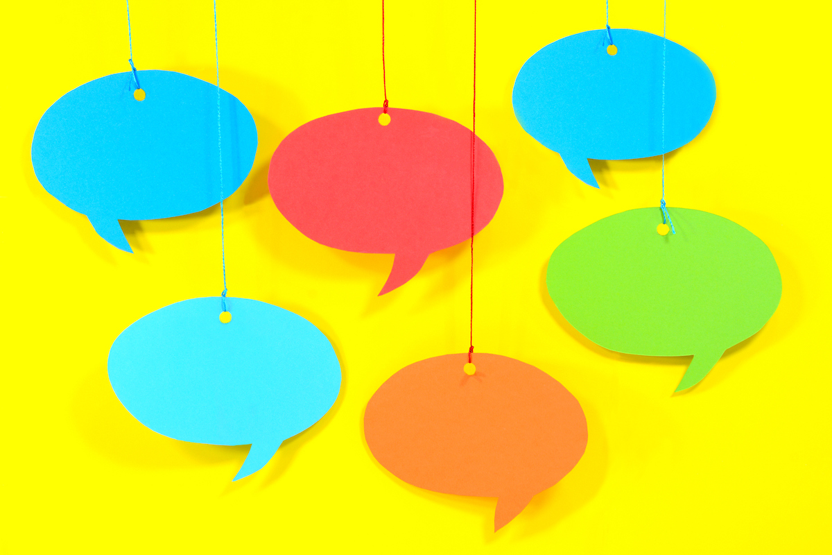 Multicolored paper speech bubbles hanging from yarn across a yellow background.