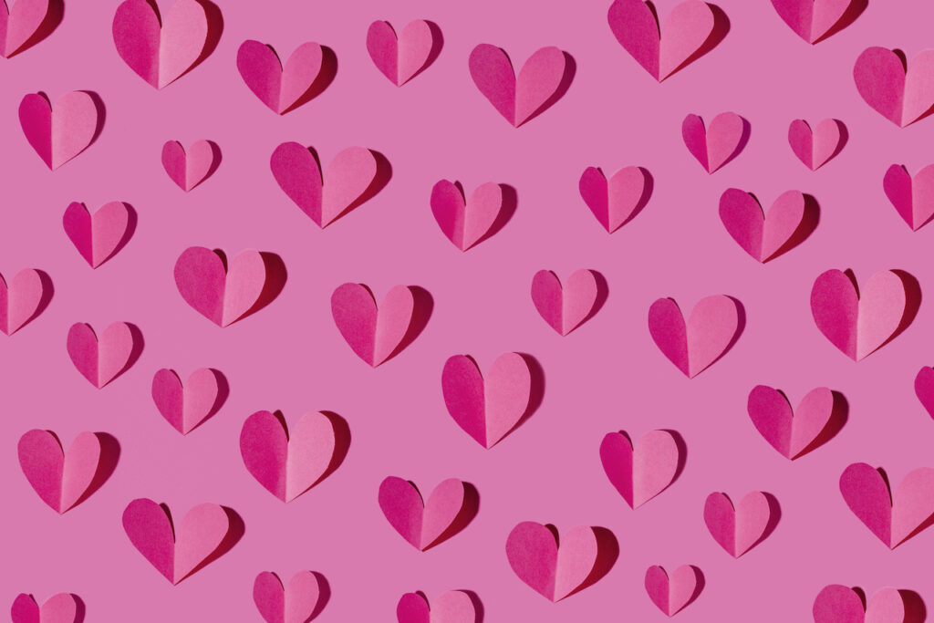 Folded pink paper hearts are arranged on a pink background.