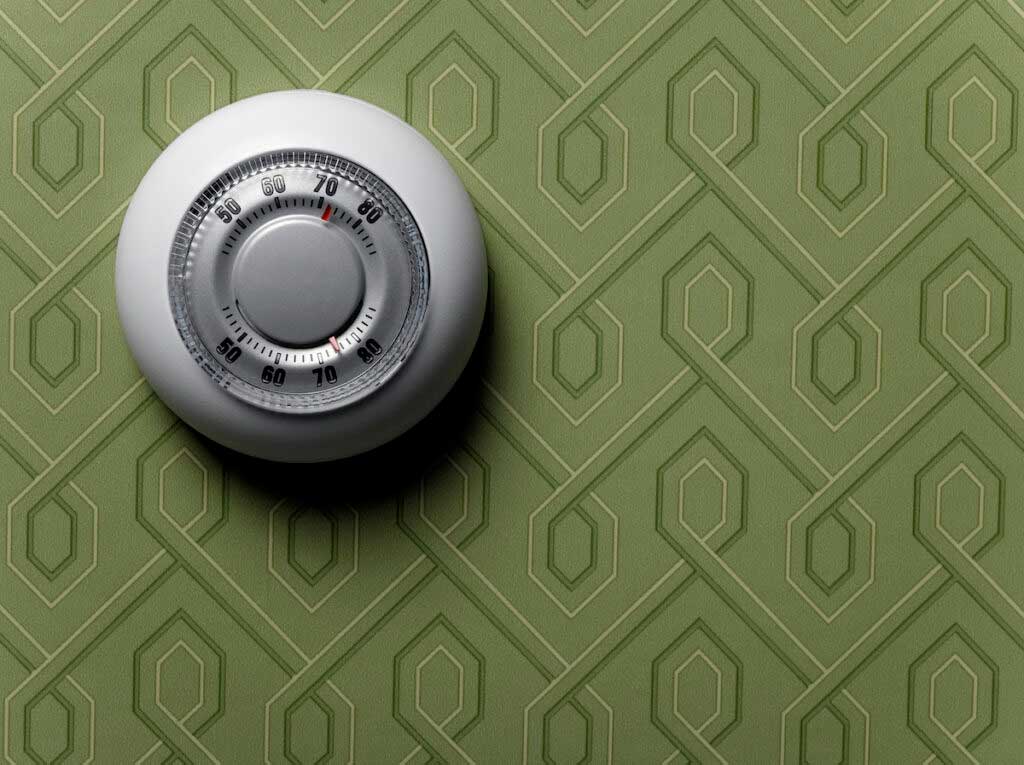 A thermostat against green vintage wallpaper.