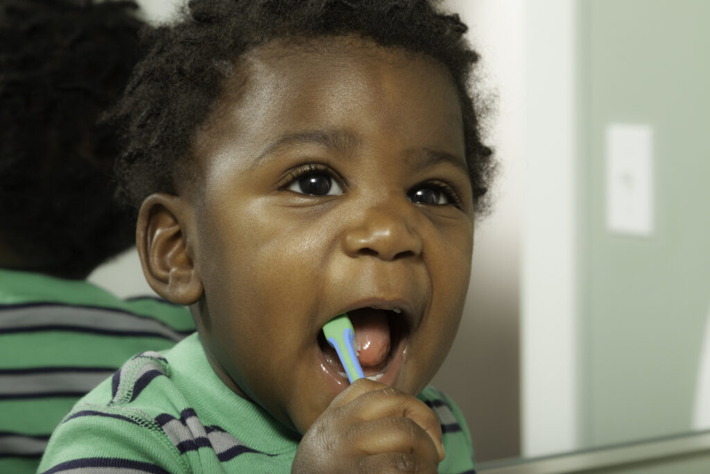 A toddler bushes their teeth in front of a mirror.