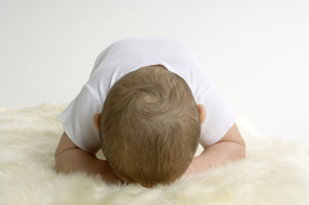 A baby rests face down on a fuzzy blanket during tummy time.