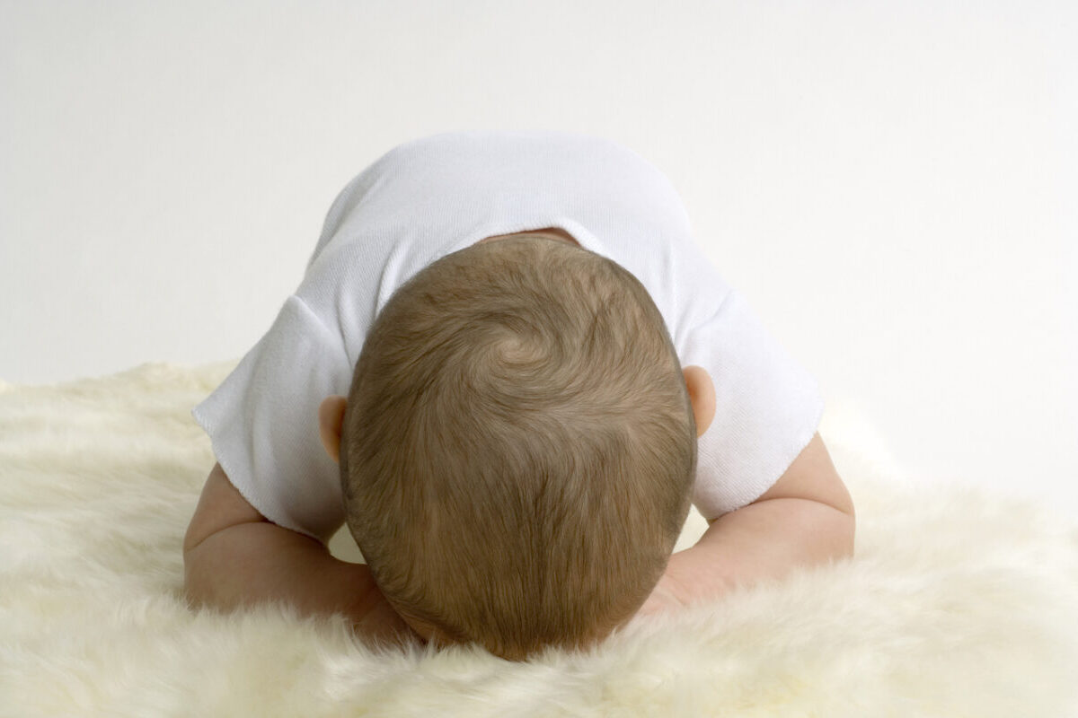 A baby rests face down on a fuzzy blanket during tummy time.