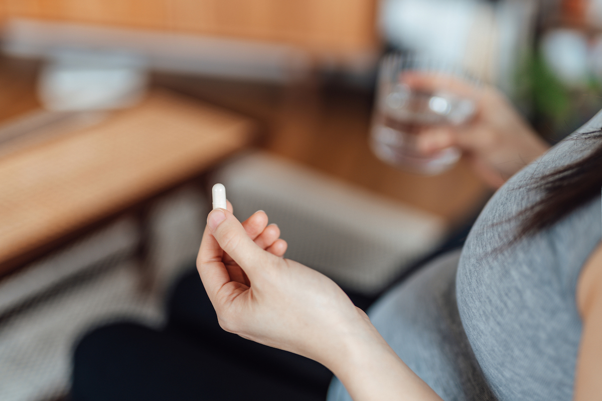 A close-up of a pregnant person holding a white pill and glass of water.