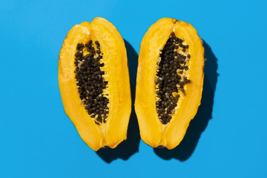 An overhead view of a sliced papaya with seeds on a blue background.