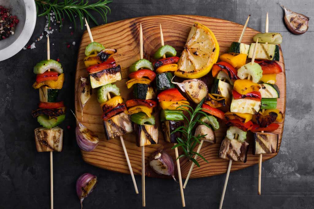 Skewers of grilled vegetables are arranged on a wooden tray.