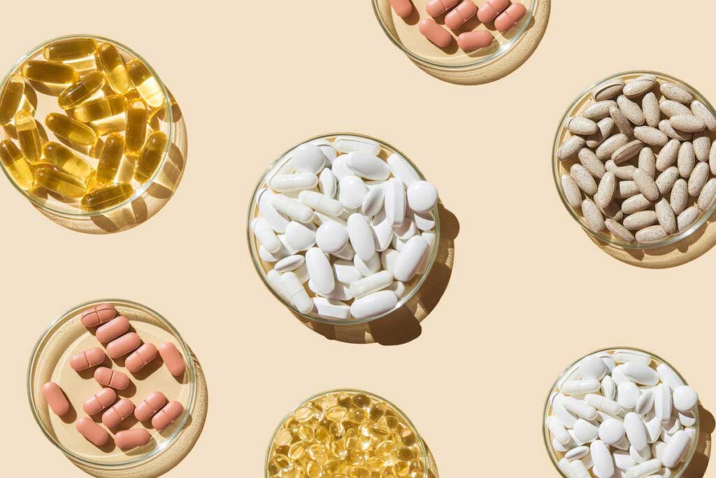 Bowls of various pills and capsules on a light pink background.