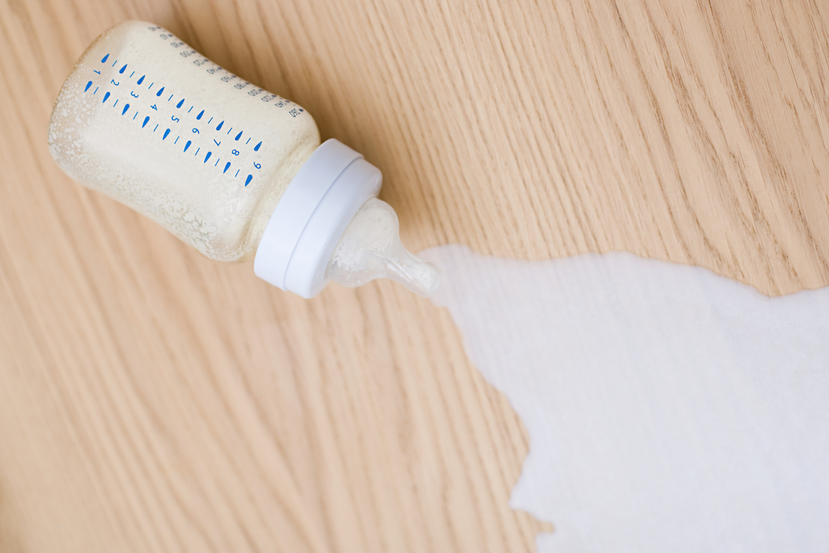 A tipped bottle spills milk across a wood table.
