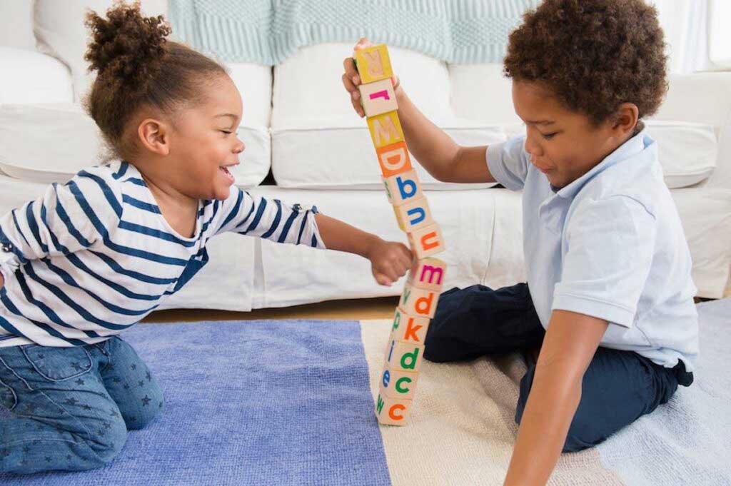 One child stacks block while another knocks the tower over.