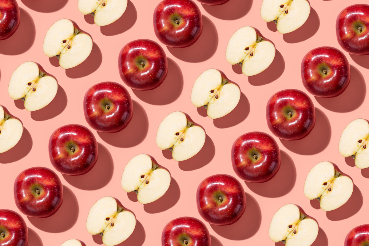 Sliced red apples arranged in stripes on a pink background.