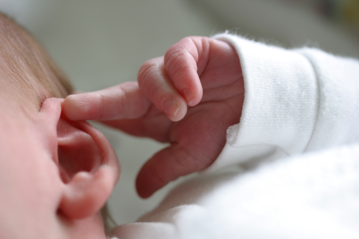 A closeup of a newborn touching their ear.