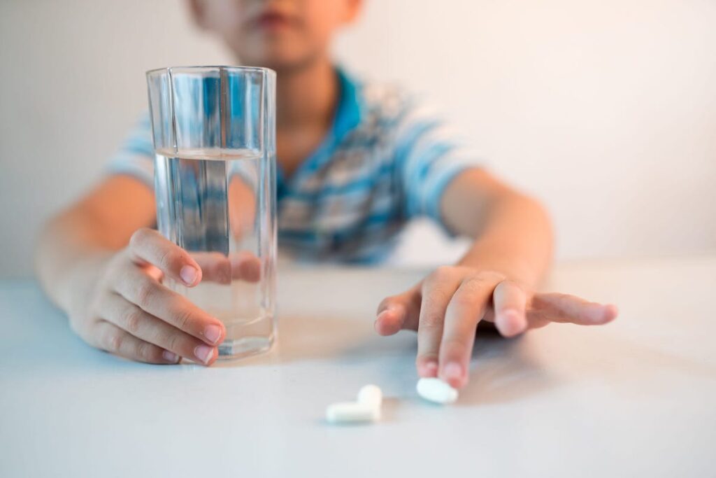 A young child touches probiotic pills while holding a glass of water.