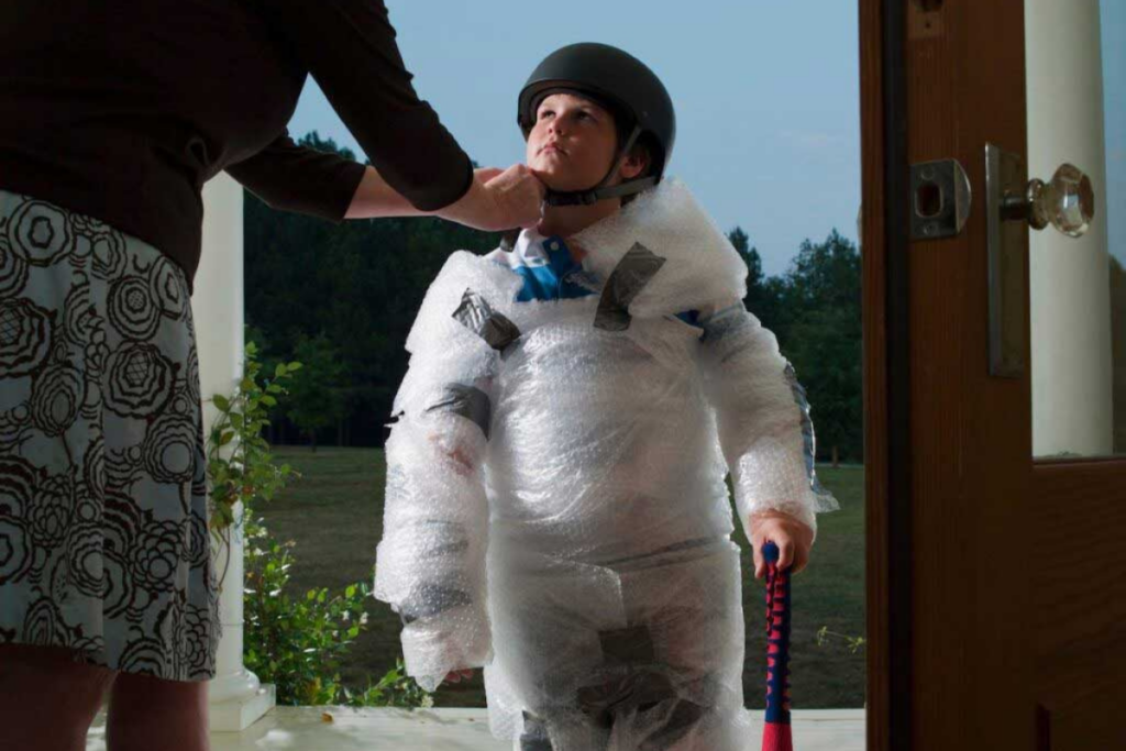 A child prepares to go out to play by getting wrapped in bubble wrap and wearing a helmet.