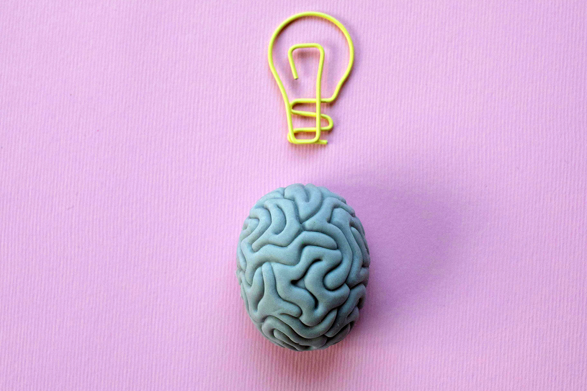 A small figurine of a brain with a yellow light bulb paper clip above it.