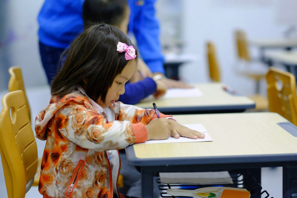 a kid sitting in school desk and writing on a paper