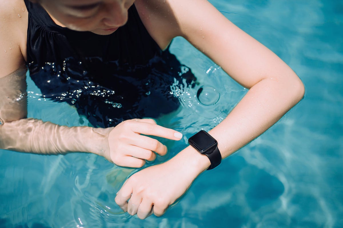 A swimmer stands in a pool while looking at the screen of her wearable tracker watch.