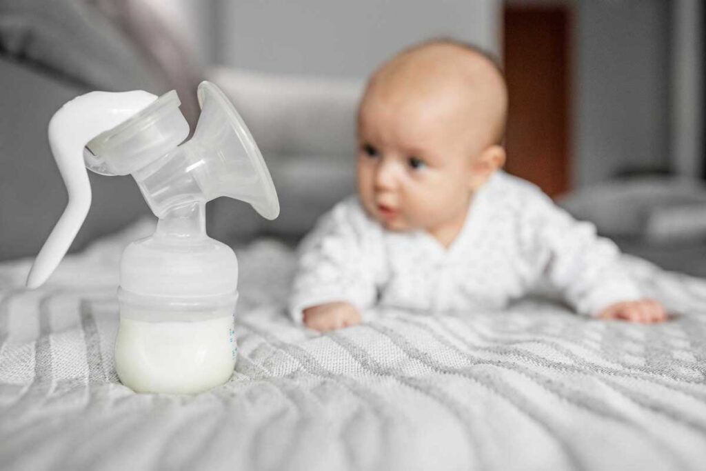 A baby on its tummy looks over at a full bottle attached to a manual breast pump.