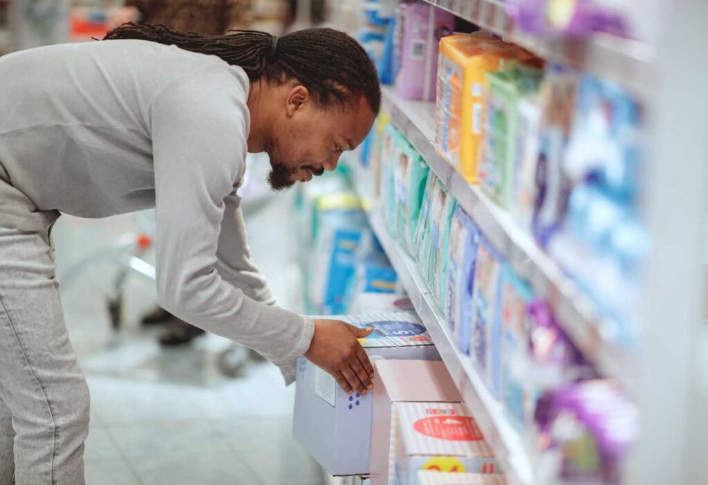 Shopper bends down to pick up a box of diapers in the diaper aisle of a big-box store.
