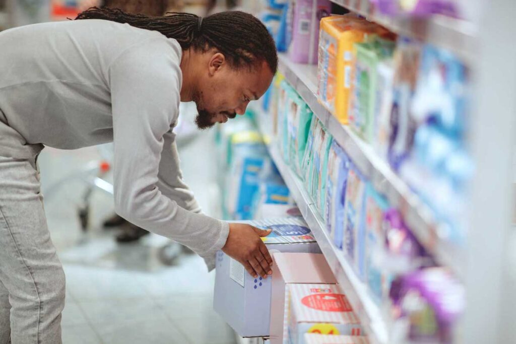 Shopper bends down to pick up a box of diapers in the diaper aisle of a big-box store.