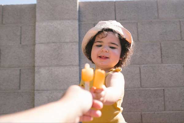 Denisse Myrick's daughter holds a popsicle and does "cheers" with her mother's popsicle.
