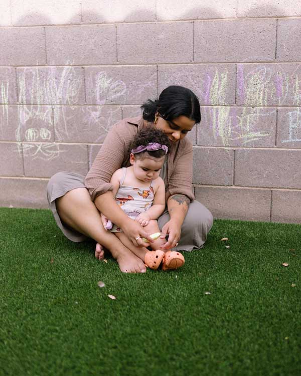Denisse Myrick sits with her daughter in the green grass.