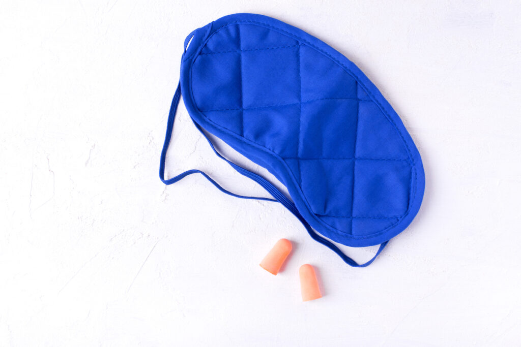 A blue sleep mask and orange ear plugs sit on a white marble countertop.
