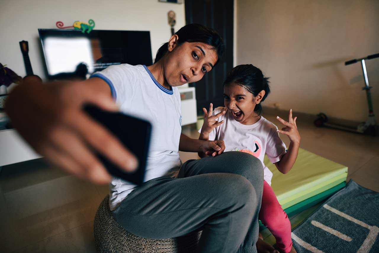 A parent and child make funny faces while taking a selfie in their living room.