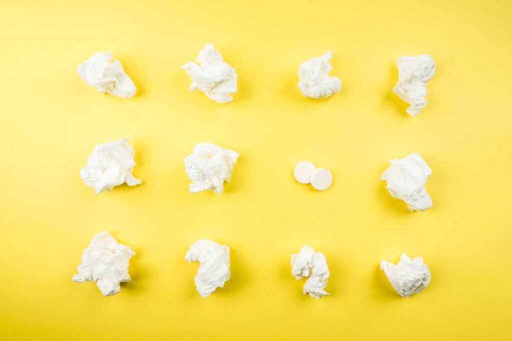 An array of used tissues and cold medicines on a yellow background.