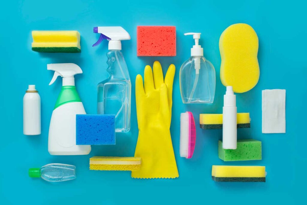 Household cleaning products, rubber gloves, soap, and scrub brushes are arranged on a teal background.