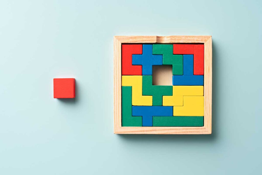 A colorful wooden children's block puzzle is seen on a light blue background. The last piece is set outside the puzzle.