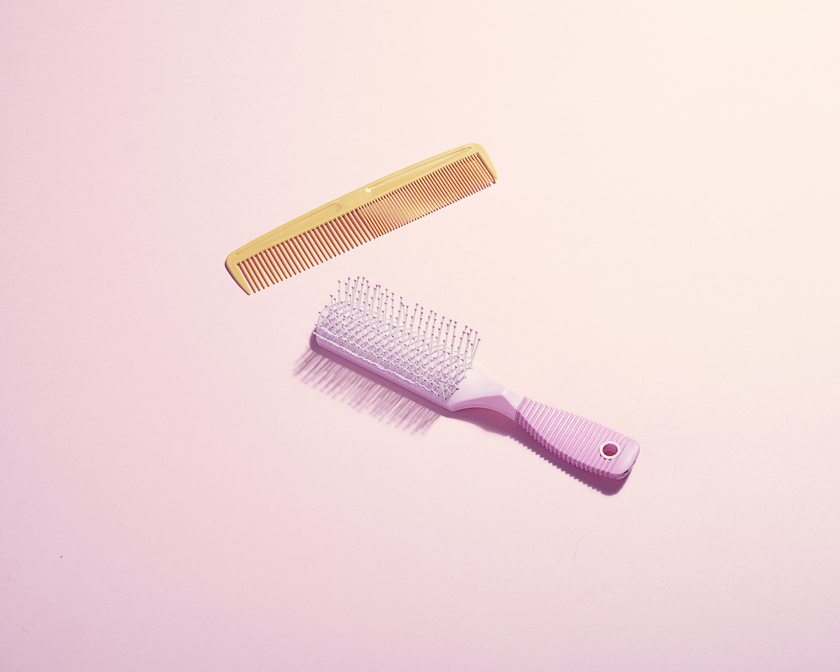 A pink hairbrush and yellow comb on a light pink background.