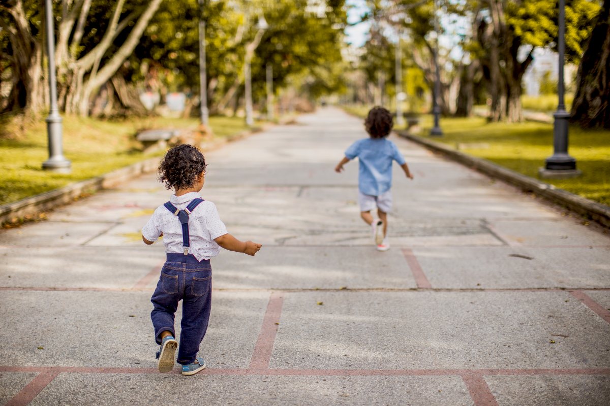 Two dark-haired toddlers run freely down a path in a park.