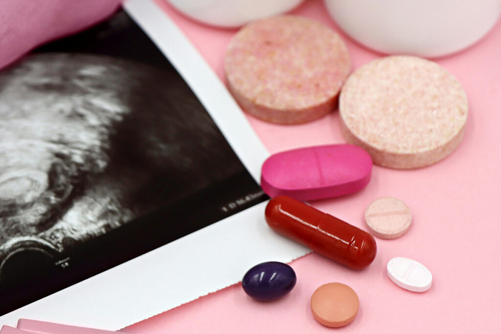 Assorted vitamins and pills on an ultrasound and pink background.