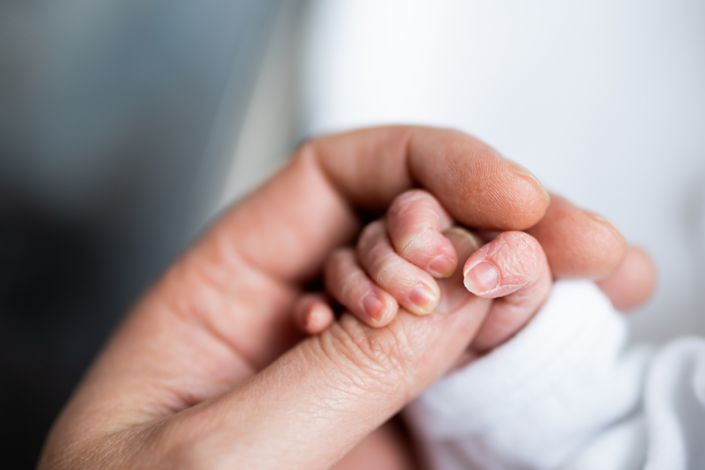 A newborn infant holds a parent's thumb in a closeup.