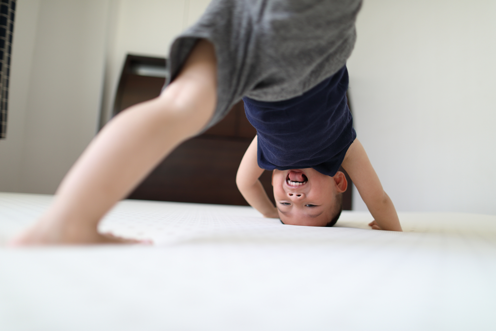 A young child tries to do a headstand on a white mattress.