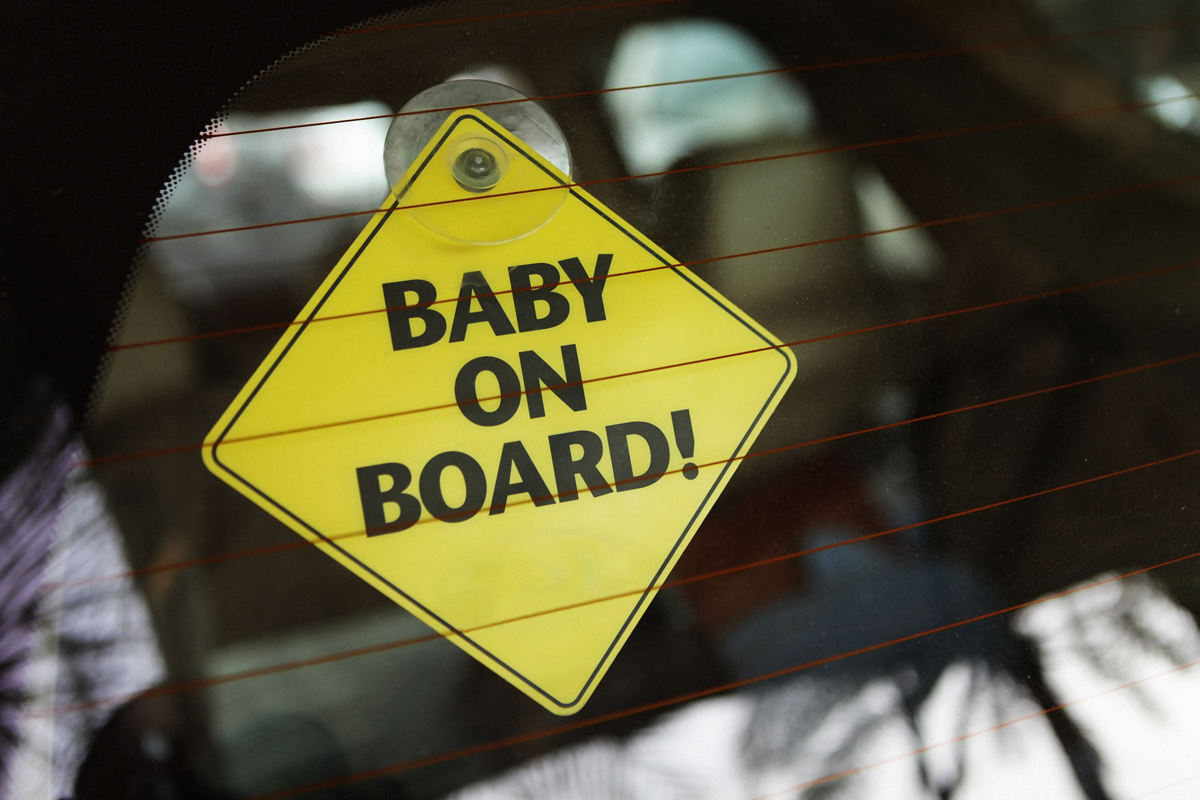 A "baby on board" sticker is seen in the rear window of a car.