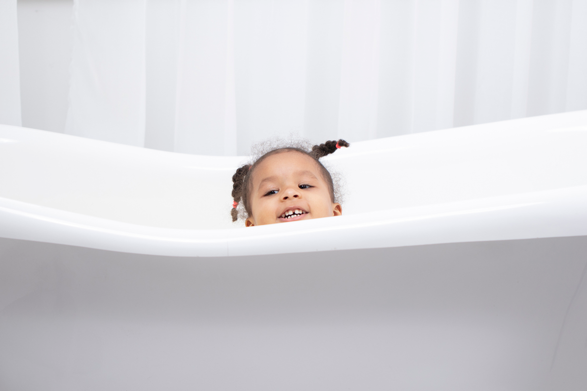 A small child smiles as they peep over the side of a white bathtub.