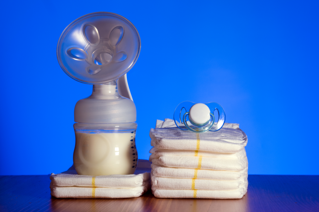 A breast pump and full bottle of milk sit on a stack of diapers against a blue background.