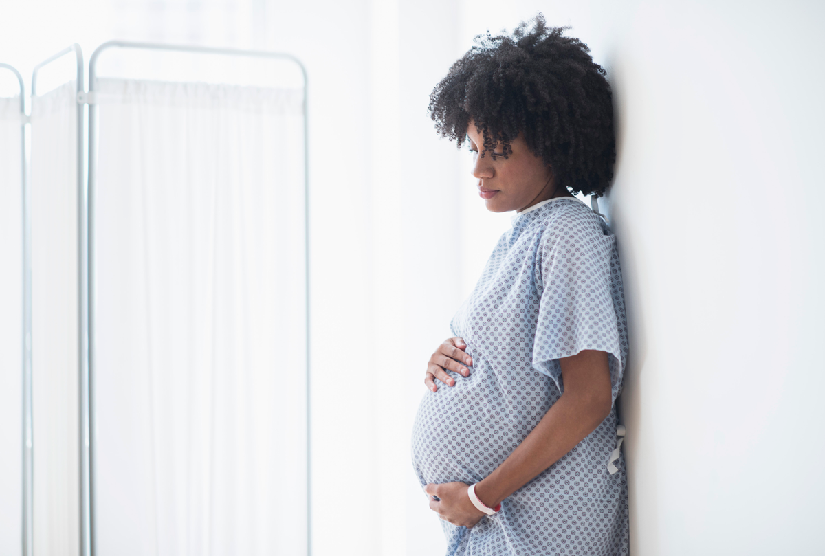 A pregnant person leans against the wall in the labor&delivery unit of the hospital.