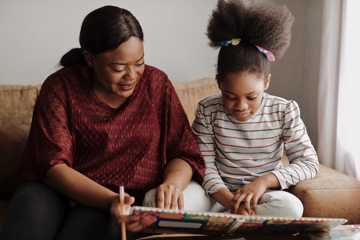 A parent and child look at a book during a homeschool reading session.