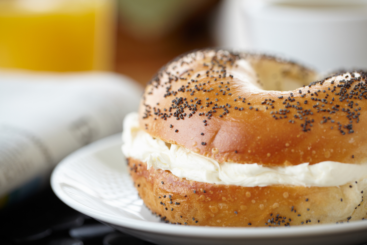 A close-up of a poppy seed bagel with cream cheese.