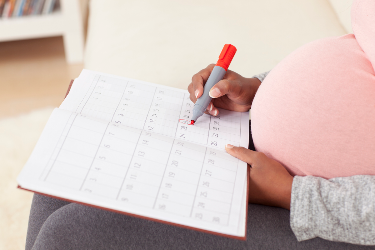 A view of a pregnant person circling a date in a calendar.