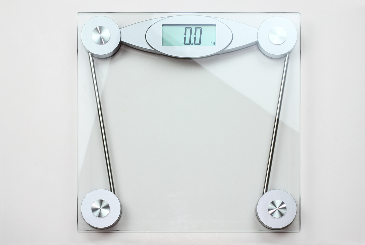An overhead view of a clear glass digital scale on a white background.