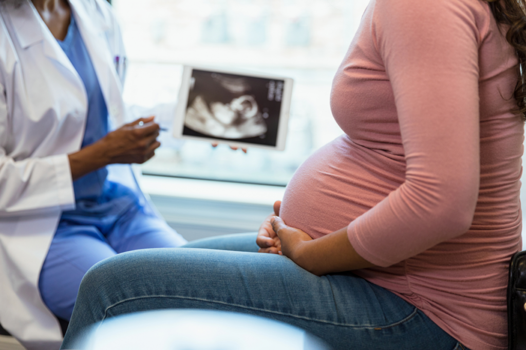 A close up of a doctor pointing to an ultrasound and a pregnant person holding their stomach.