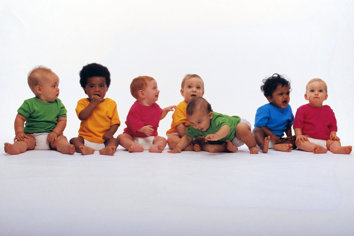 A row of baby boys in green, yellow, red, and blue shirts, with assorted emotions.