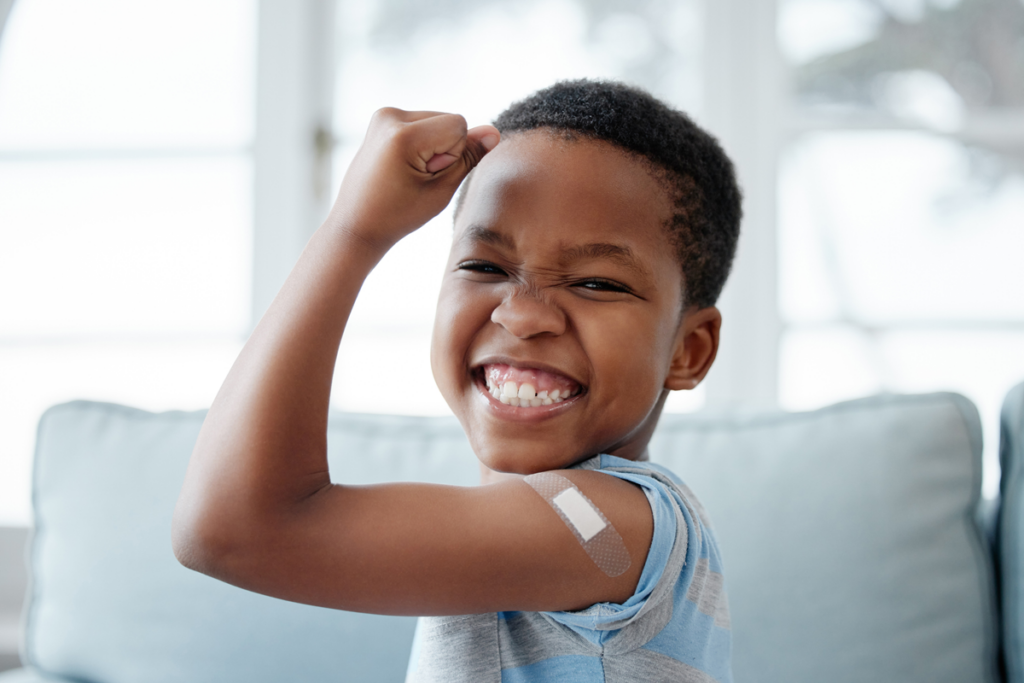 Smiling young child flexes and shows of a bandaid from a recent vaccination.