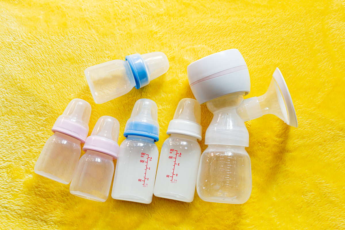 Bottles of breast milk and a breast pump are arranged on a yellow cloth.